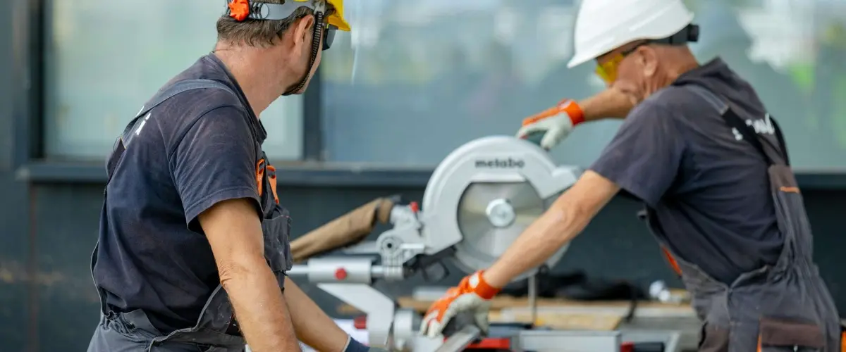 Two professionals in a construction setting, one wearing a yellow hard hat and the other smiling.